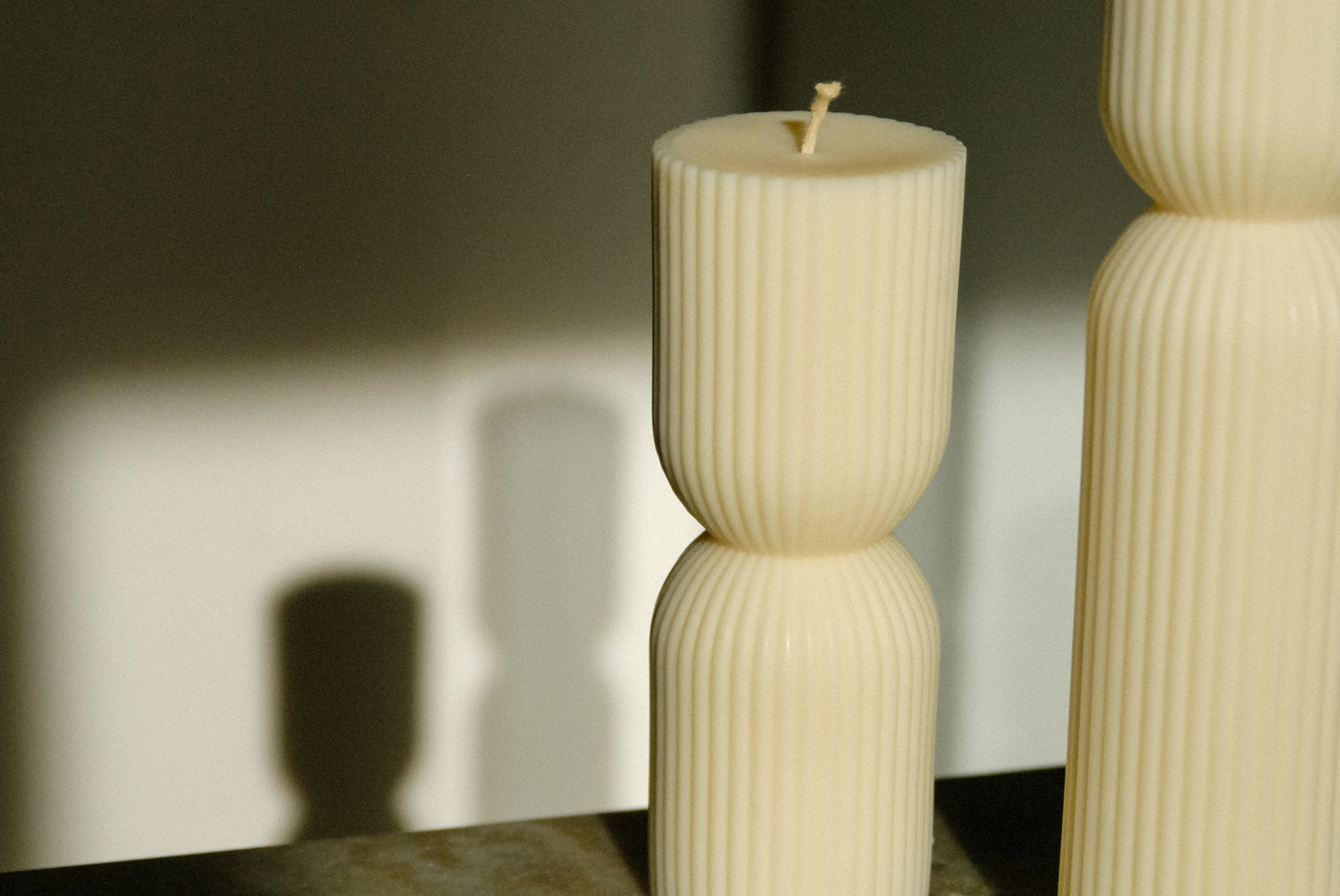 Zwei Stumpenkerzen in weiß mit Riffeln werden von der Sonne angestrahlt.