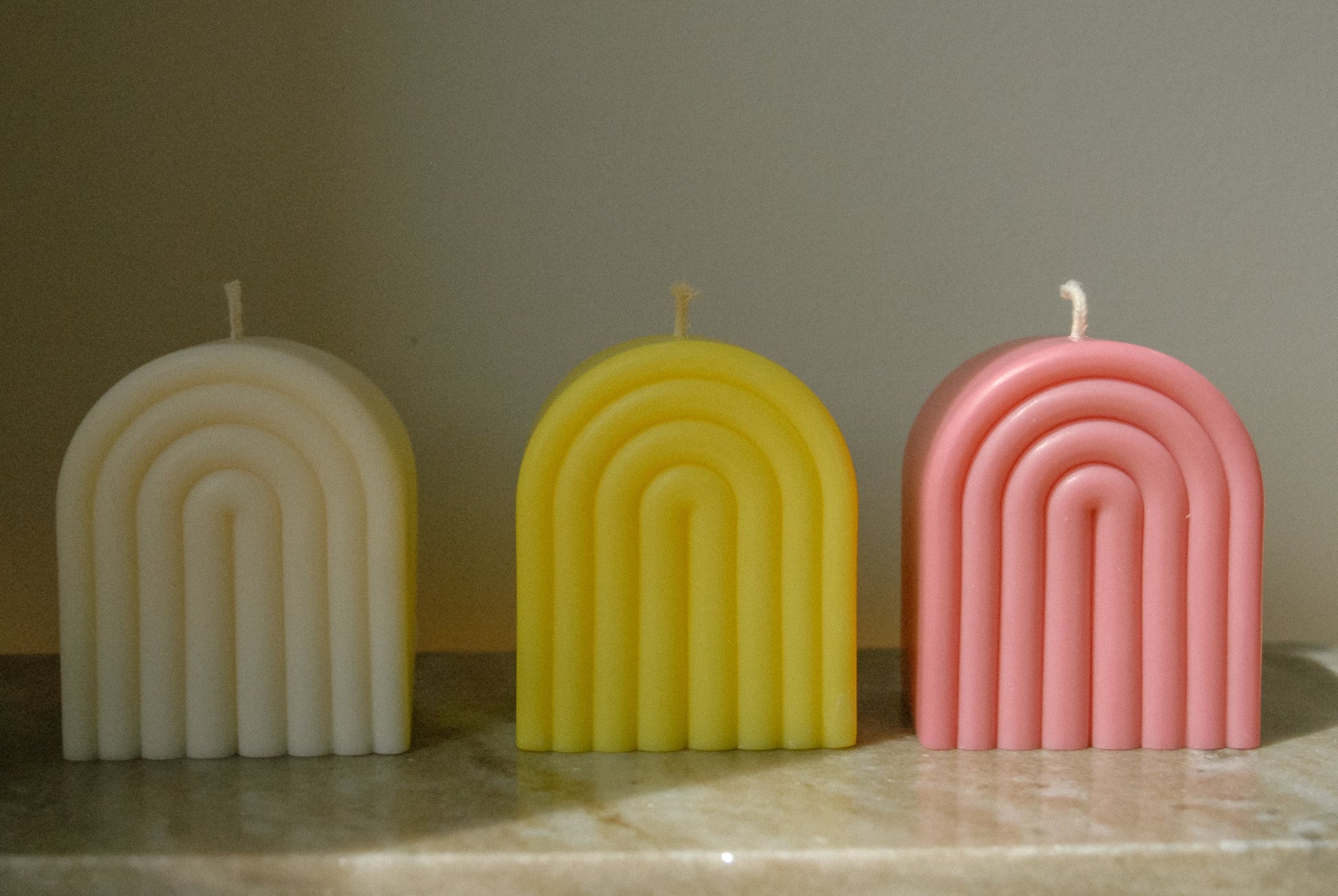 Drei Kerzen in Form eines Regebogens in weiß, gelb und rosa
