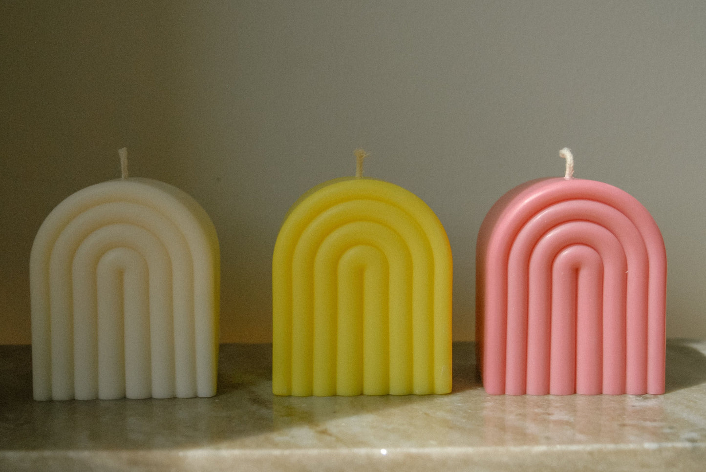 Drei Kerzen in Form eines Regebogens in weiß, gelb und rosa